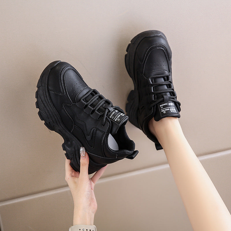 Black sneakers held by a person against a neutral background