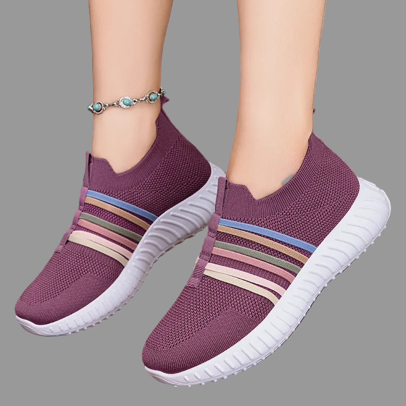 Purple sneakers with colorful stripes worn by a person on a wooden floor.