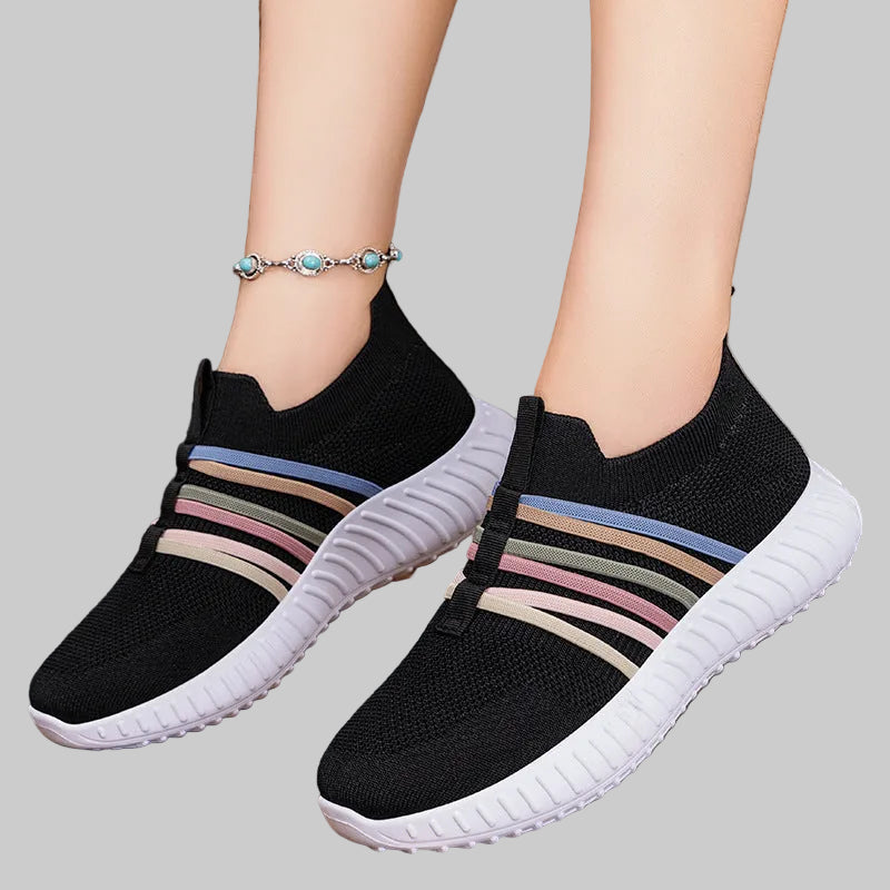 Black slip-on sneakers with colorful stripes on a wooden floor