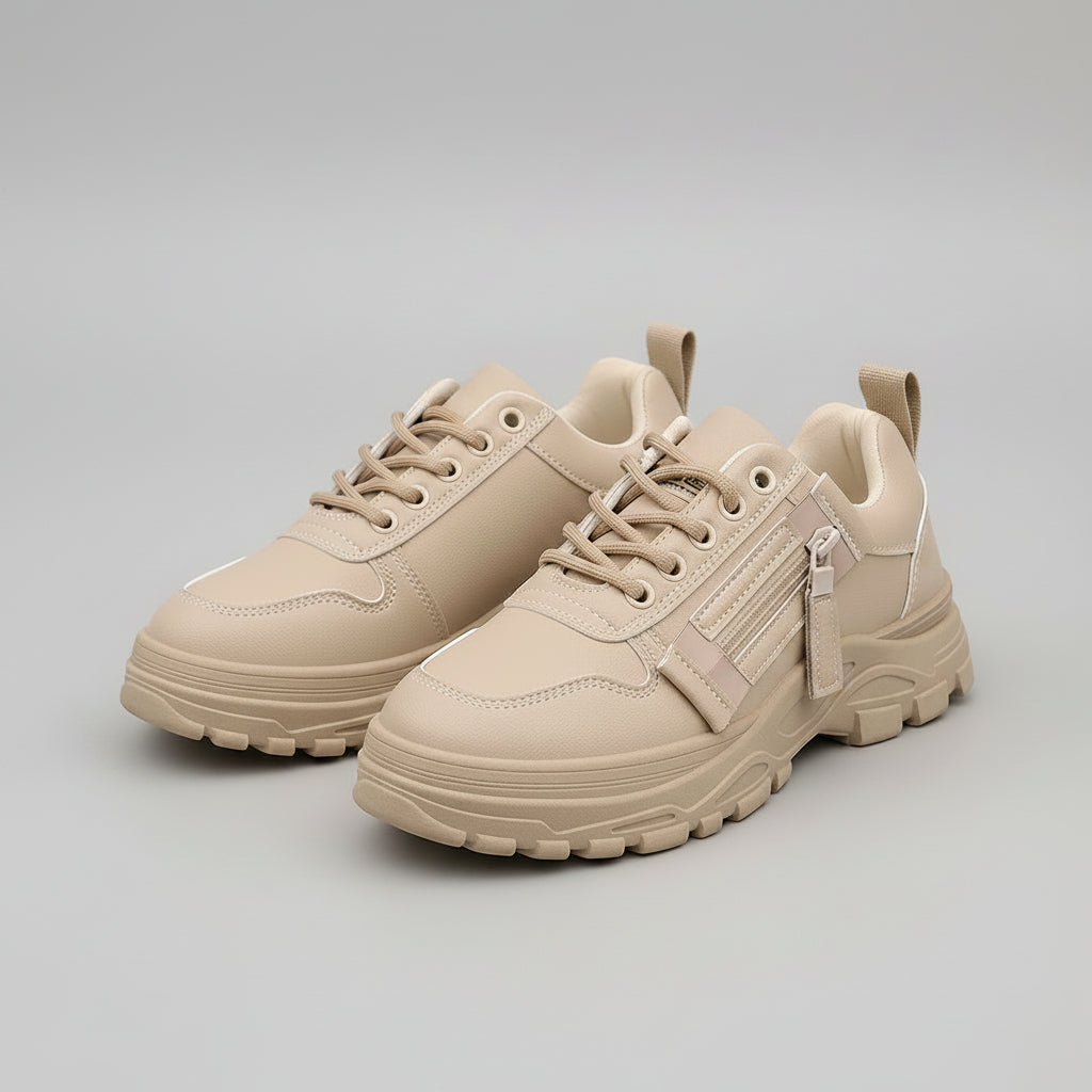 Beige sneakers with visible branding held by a hand on a pavement background