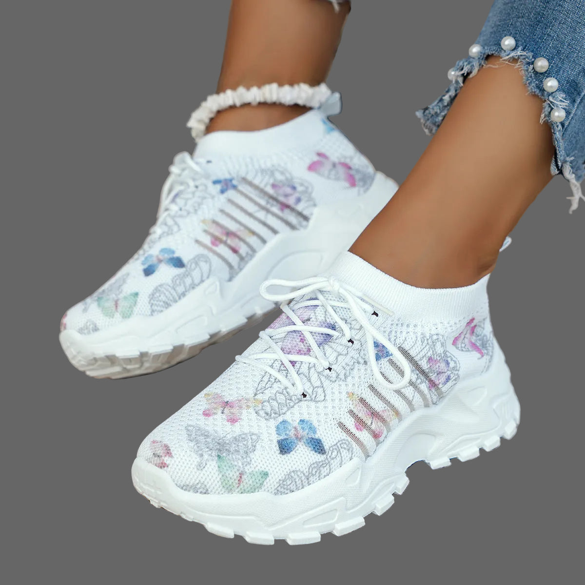 White sneakers with butterfly patterns worn by a person on a woven surface