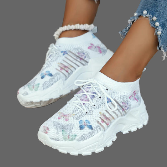 White sneakers with butterfly patterns worn by a person on a woven surface